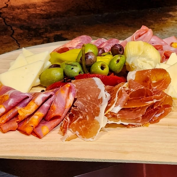 A wooden board filled with various cured meats, cheeses, olives, and pickled vegetables.