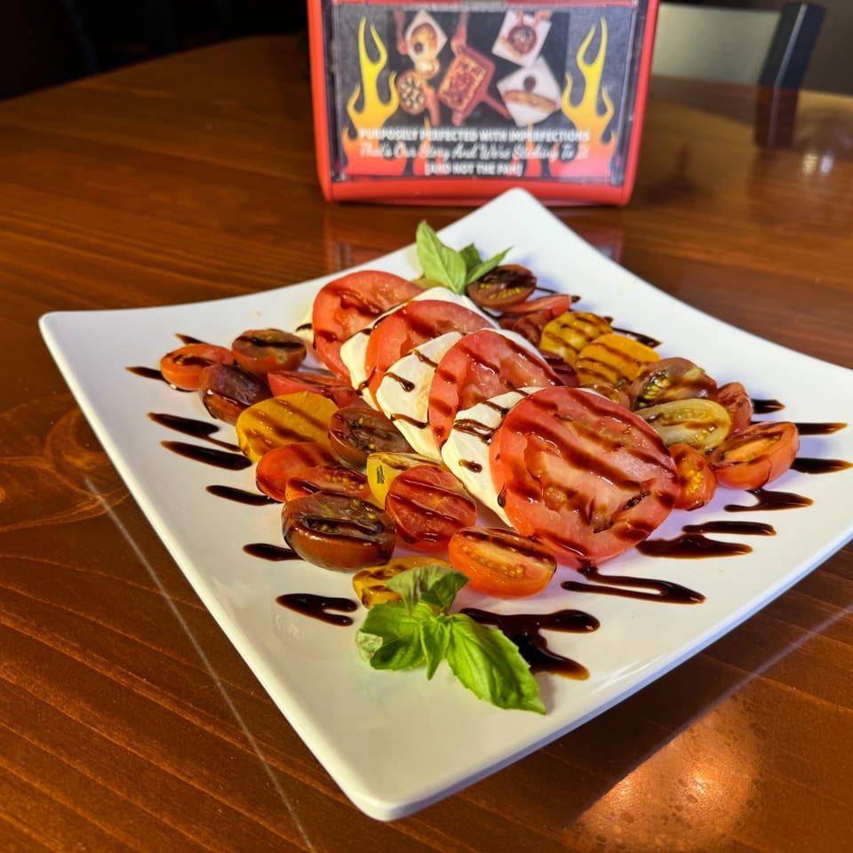 Caprese salad with sliced tomatoes, mozzarella, basil, and balsamic glaze on a white plate.