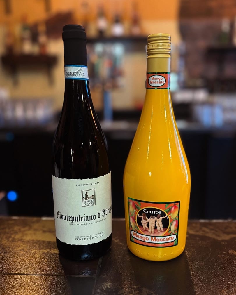 Two bottles, Montepulciano d'Abruzzo red wine and yellow Mango Moscato, on a bar counter.