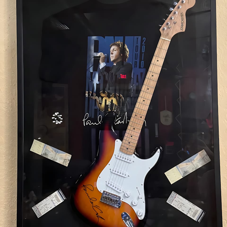 Framed Paul McCartney 2010 tour memorabilia featuring a signed guitar, t-shirt, and concert tickets.