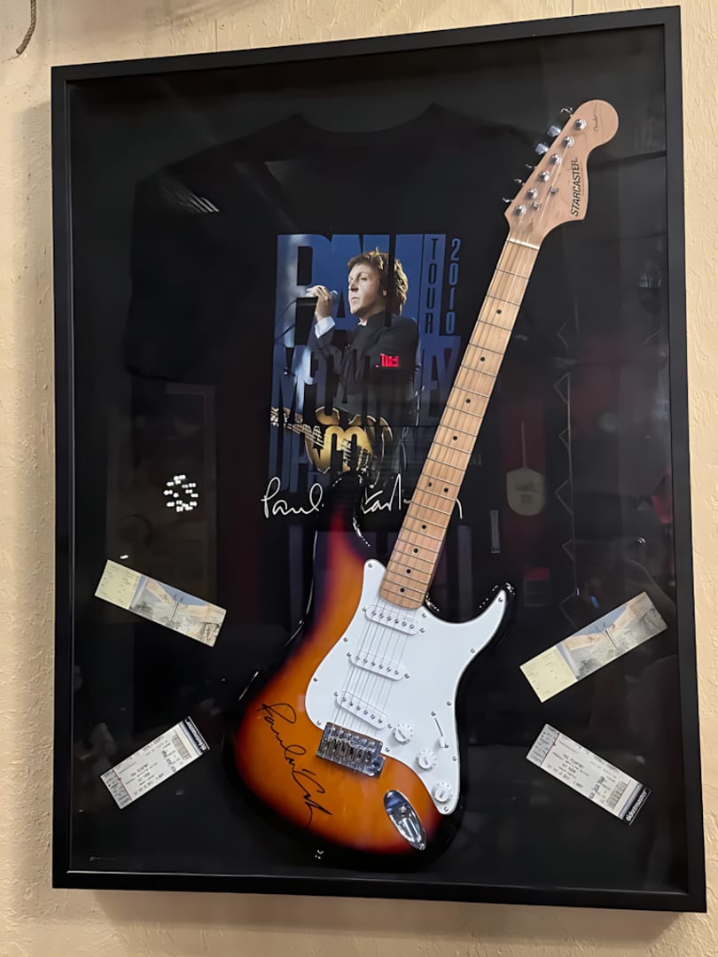 Framed Paul McCartney 2010 tour memorabilia featuring a signed guitar, t-shirt, and concert tickets.