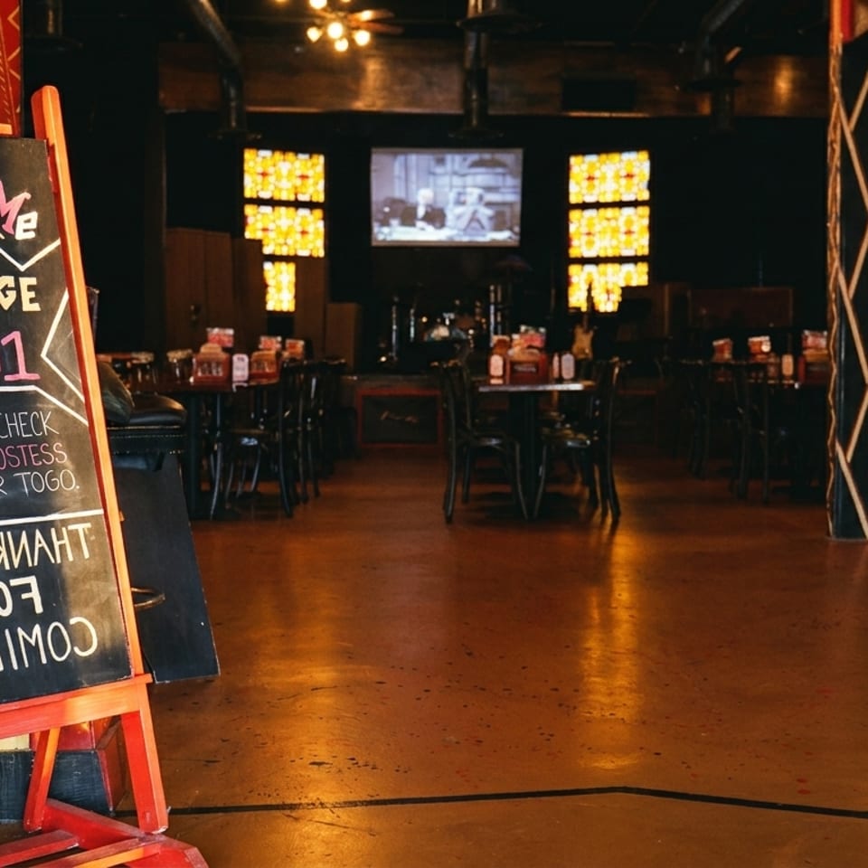 A welcome sign for Stage 201 stands in a dimly lit restaurant with tables and a stage.