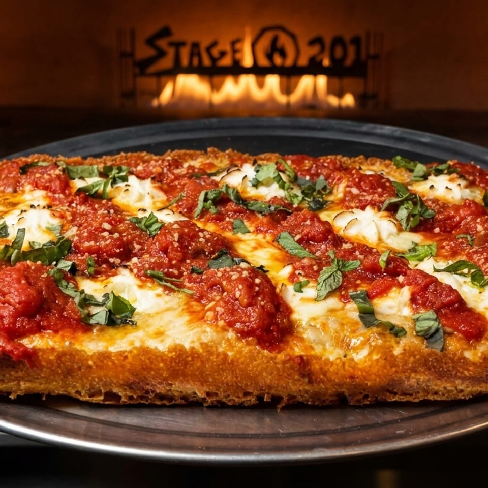 A rectangular Detroit-style pizza with red sauce, white cheese, and basil, held in front of a pizza oven.