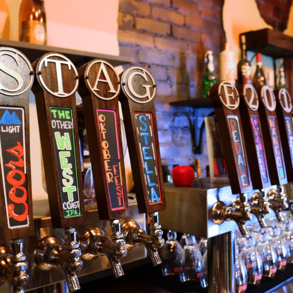 Close-up of multiple beer taps with various brand names like Coors, West, Oktoberfest, and Stella.