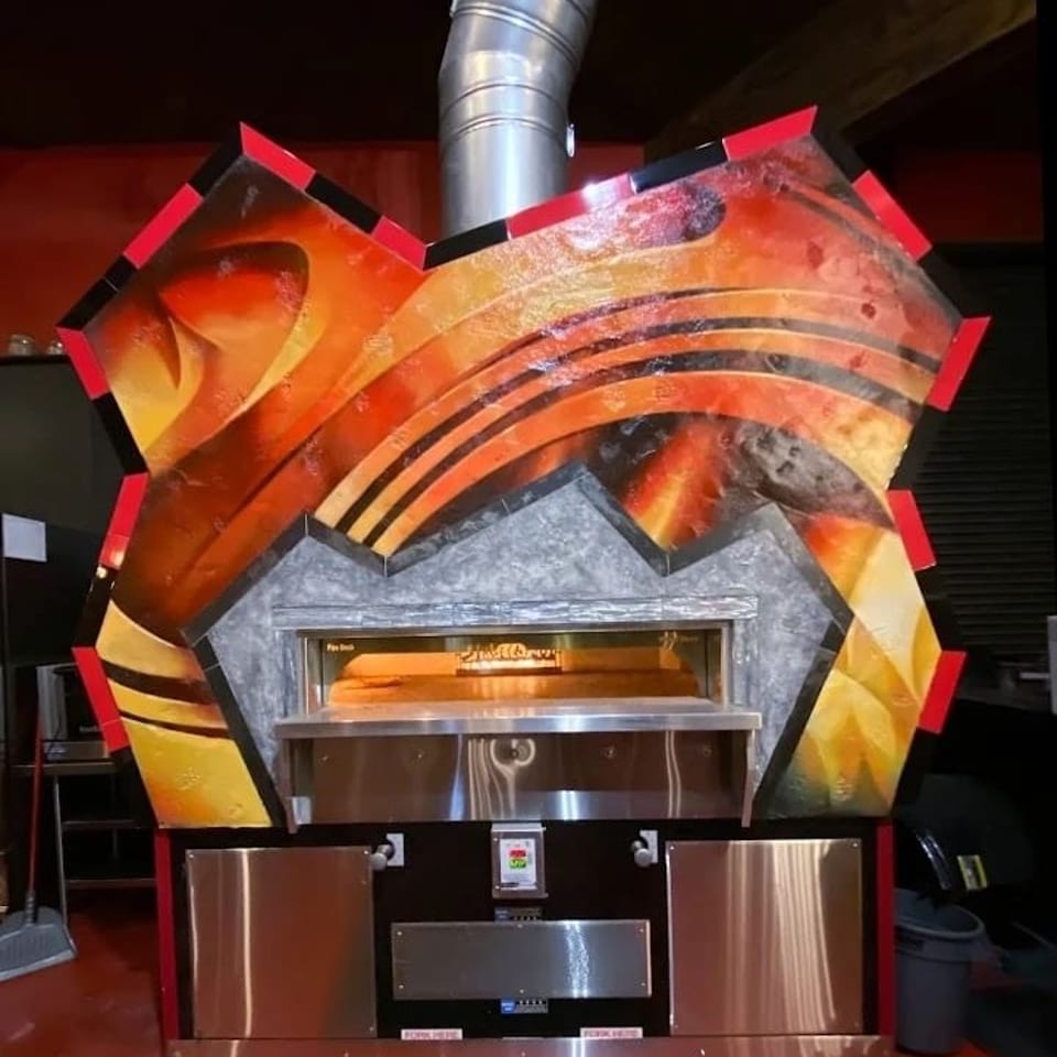 Commercial pizza oven with a vibrant, flame-inspired artistic facade and stainless steel base.