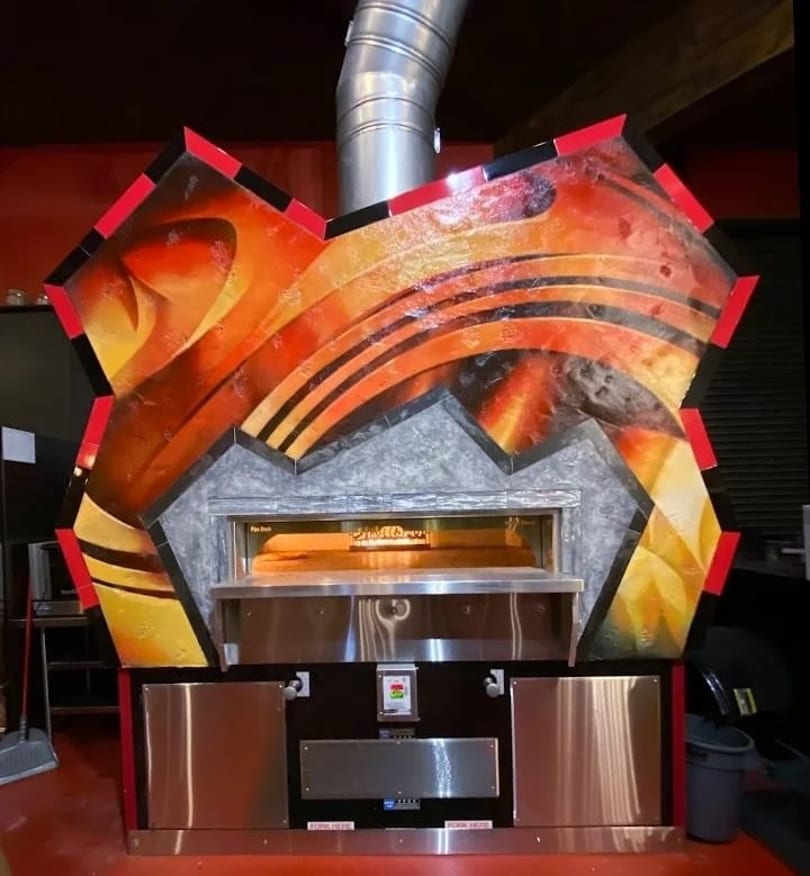Commercial pizza oven with a vibrant, flame-inspired artistic facade and stainless steel base.