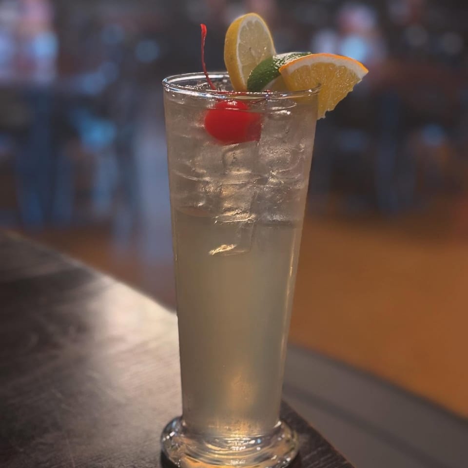 Refreshing iced cocktail with lemon, orange, cherry, and mint on a dark bar top.