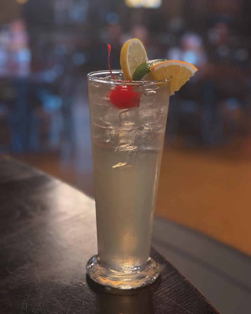 Refreshing iced cocktail with lemon, orange, cherry, and mint on a dark bar top.